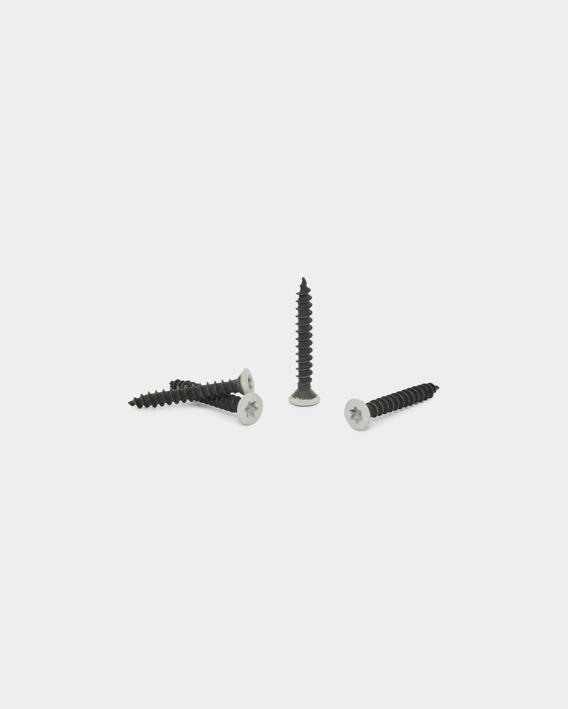 WoodUpp wood screws: four black, coarse-threaded wood screws with bright silver flat countersunk heads and cross recesses arranged on a white background — three lying horizontally and one standing upright, photographed close-up to show threading and head detail. This WoodUpp product shot emphasizes build quality and corrosion-resistant head finish.