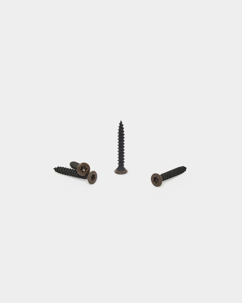 WoodUpp: four dark brown/black wood screws on a white background — three lying flat and one standing upright. Each WoodUpp screw has a countersunk, star/Phillips-style head with coarse threads, a black-coated threaded shaft and a slightly brown, flat head finish.