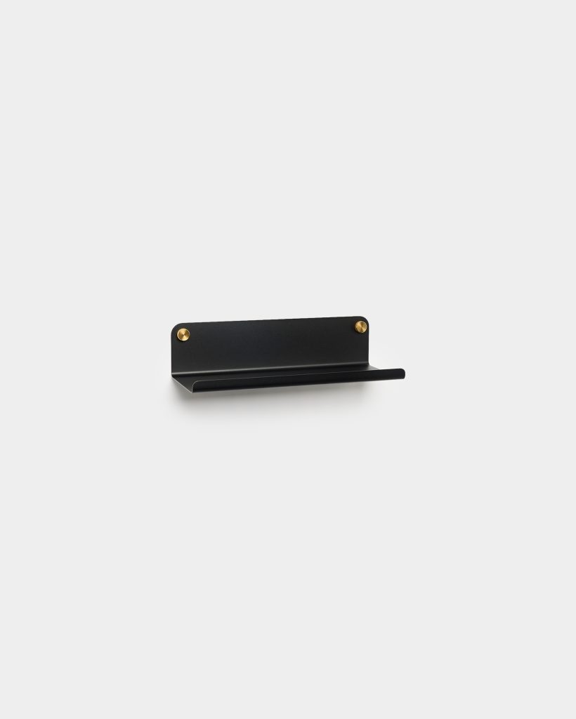 WoodUpp small matte black metal wall shelf displayed against a white background, featuring a slim horizontal ledge with upturned front lip and two visible round brass mounting screws—minimal, modern design ideal for holding small items like phones, keys, or toiletries.