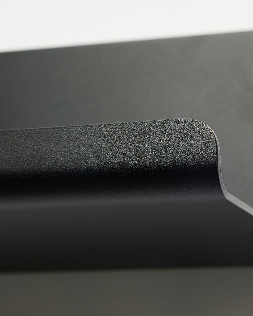 Close-up of a WoodUpp black powder-coated steel monitor arm clamp, showing the textured matte finish and rounded lip of the curved bracket. The image highlights the smooth radius, subtle edge detailing and sturdy minimalist design of the WoodUpp desk mount component.