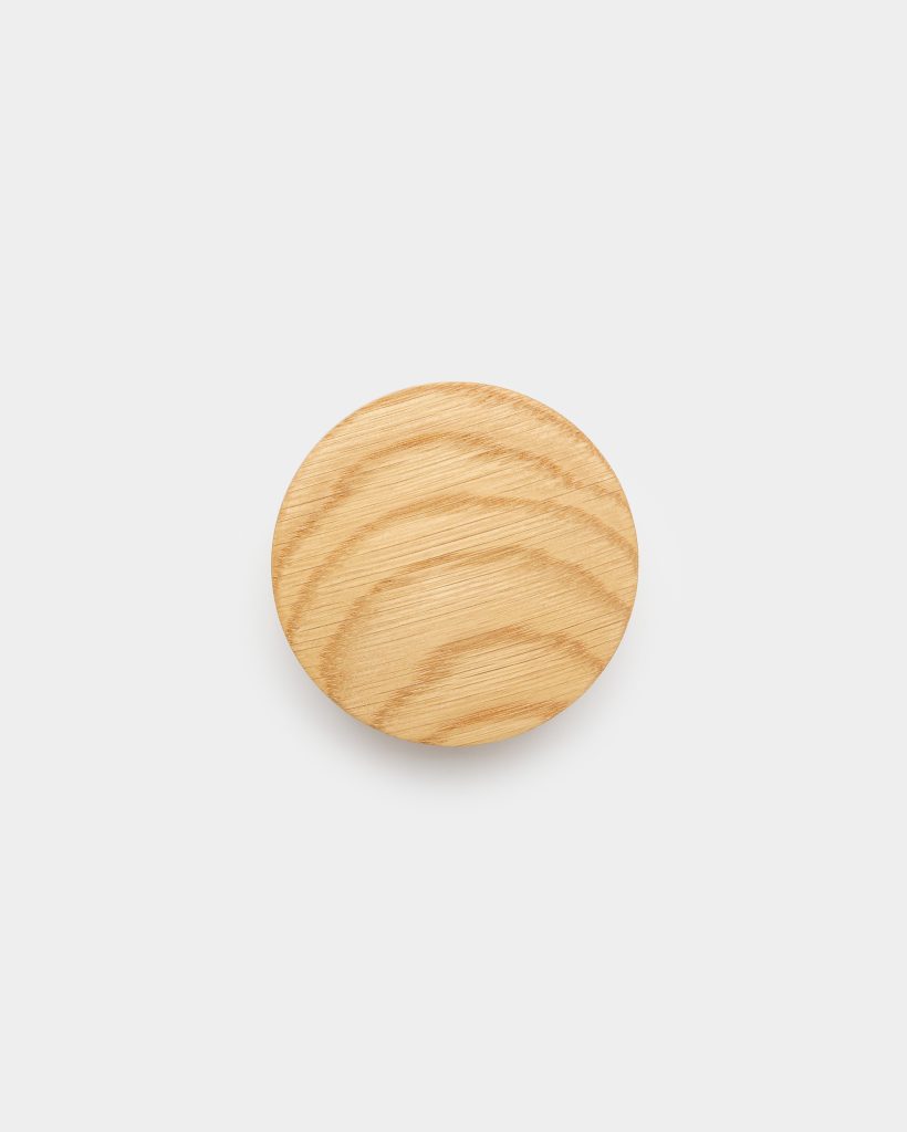 WoodUpp product: a single round wooden wall hook displayed on a clean white background. The light oak circle shows natural grain, smooth sanded surface and subtle beveled edge, casting a soft shadow beneath. Minimalist, compact design suitable as a coat hook or decorative knob.