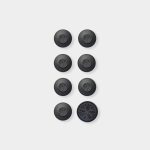 WoodUpp: eight round black adhesive rubber feet arranged in two columns on a white background. Seven small pads feature a recessed tree-logo center; one larger pad at bottom-right shows an enlarged tree pattern. The image highlights WoodUpp protective bumpers for furniture and electronics.