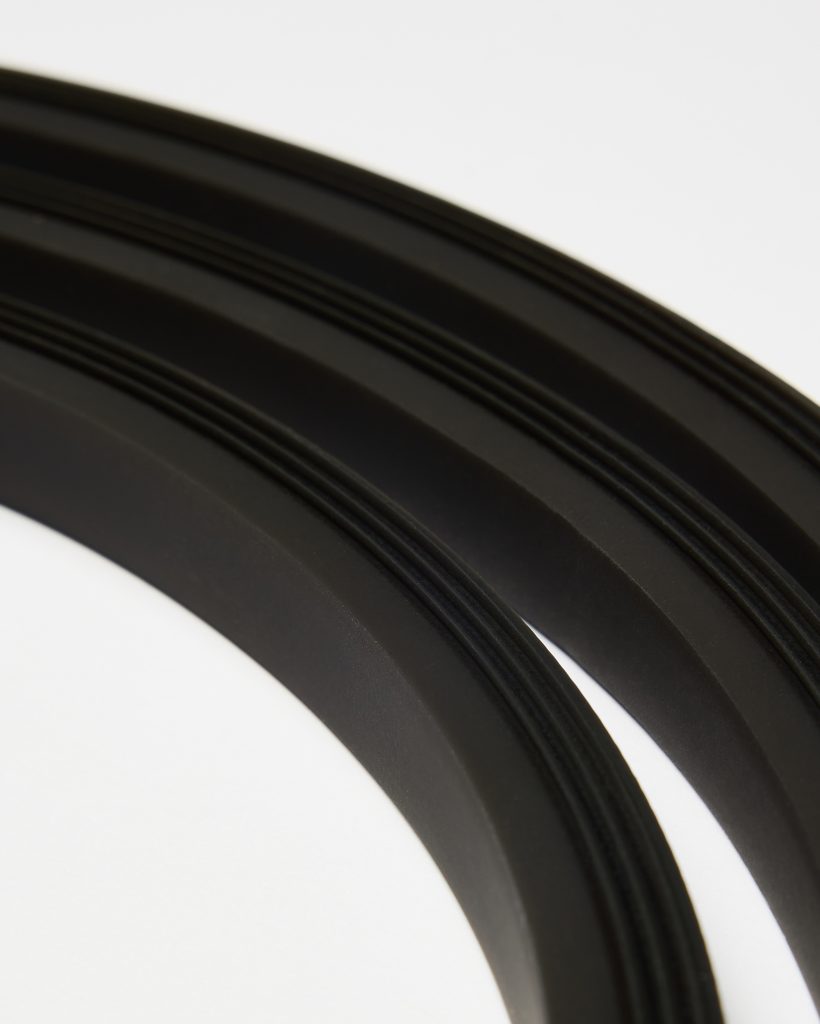 Close-up of two curved black WoodUpp trim strips displayed as arcs on a white background, showing matte-finish profiles with three parallel raised grooves along each piece; the image highlights the texture, precise edge detail, and smooth radius of these WoodUpp edging profiles.