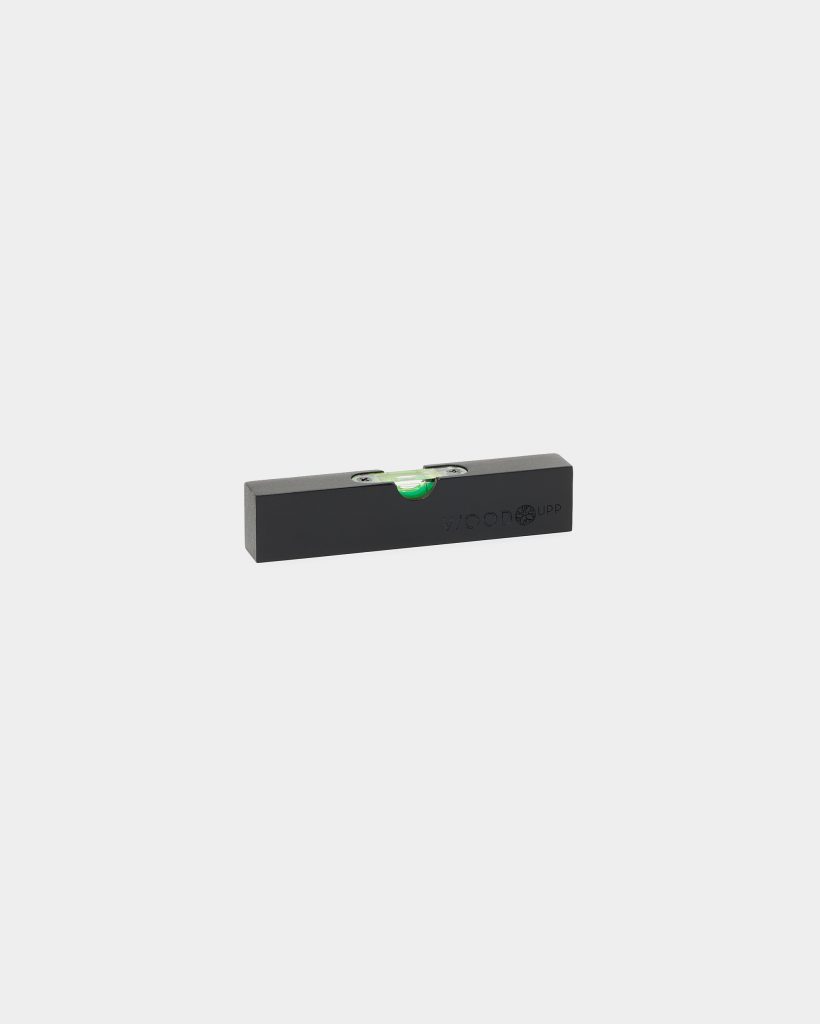 On a plain white background, a compact black WoodUpp wooden spirit level is shown — a rectangular block with an embossed WoodUpp logo, a single centered horizontal green bubble vial secured by metal brackets and visible screws. Simple, minimalist small leveling tool for accurate horizontal alignment.