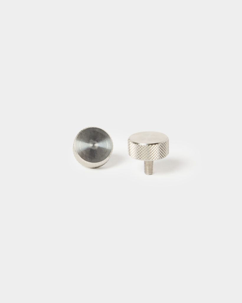 WoodUpp stainless steel knurled thumb screws shown on a white background, two small round metal knobs, one upright with a short threaded stud and the other lying flat revealing a smooth, slightly machined circular top and textured diamond knurling around the sides.