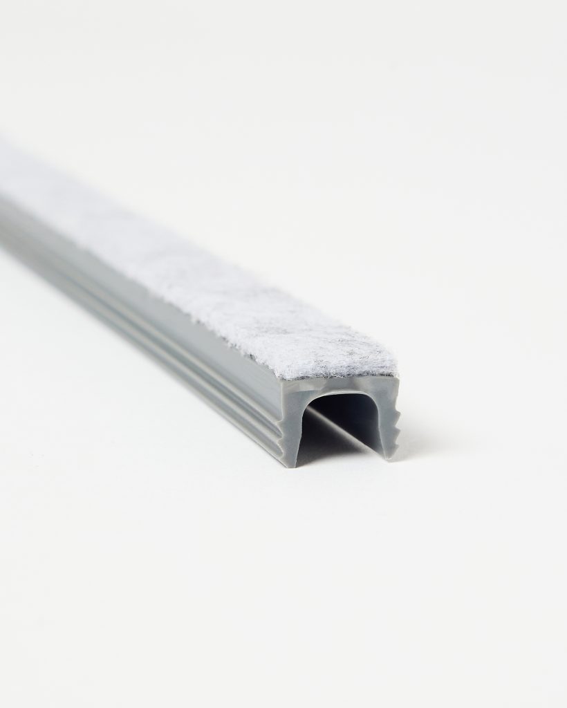 Close-up of a WoodUpp grey U-shaped rubber seal with integrated white felt strip, shown lying on a white background. The flexible WoodUpp weatherstrip features a hollow channel and adhesive felt surface designed for door or window draught exclusion and soft edge protection.