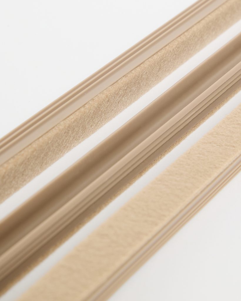 WoodUpp beige weatherstripping set showing three close-up strips: two self-adhesive felt pile seals with soft, dense fibres and a central flexible rubber bulb seal with grooved edges. The image highlights texture, profile and neutral beige color, suitable for doors and windows to block drafts.