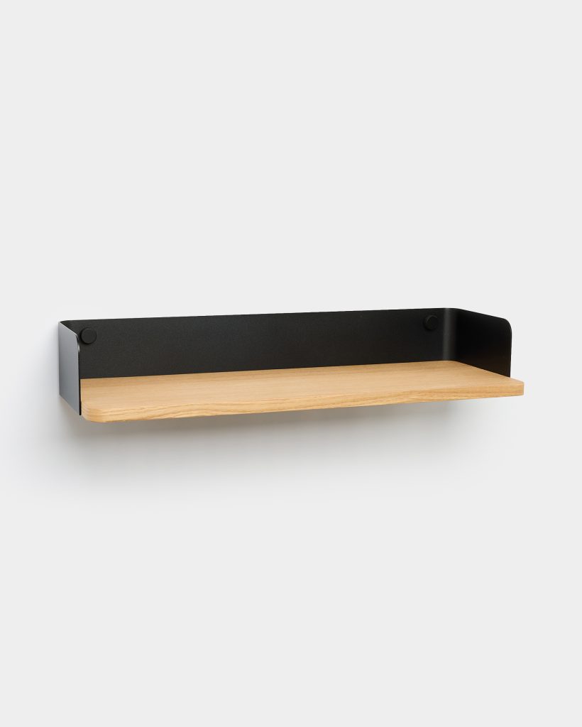 WoodUpp wall-mounted shelf: minimalist floating shelf with a light oak wooden plank resting in a matte black powder-coated steel bracket that wraps up the back and sides, secured by visible round fixings — shown mounted on a white wall, highlighting clean, modern Scandinavian design.