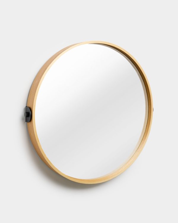 WoodUpp circular wall mirror with a slim, light oak wooden frame, mounted on a white wall by two small matte-black side brackets. The clean, minimalist mirror shows no reflection detail and highlights the natural wood grain, shallow recessed rim, and subtle shadowing around the mounted hardware.