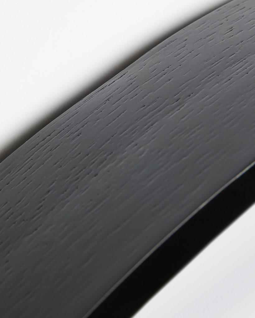 Close-up of a WoodUpp black oak finish curved wooden frame, showing the textured grain and smooth matte lacquer. The photographed WoodUpp product appears to be a black oak veneered shelf or mirror frame edge, highlighting fine wood pores and a subtle satin surface.