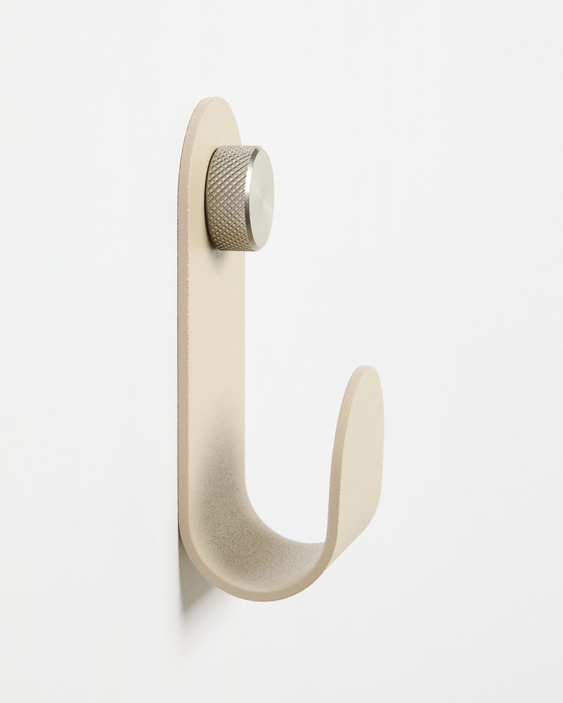 WoodUpp wall hook, a single matte beige U-shaped hook with a smooth curved profile mounted on a white wall, secured by a textured stainless-steel knurled circular mounting knob. Minimal, modern design highlighting the hook’s thickness, rounded edges and soft matte surface.