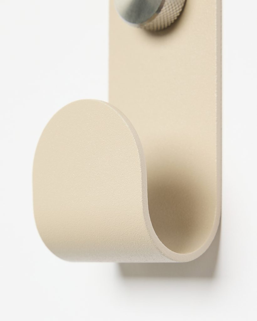 Close-up of a WoodUpp wall hook: a single, matte beige powder-coated metal loop with smooth rounded edge forming a U-shaped hanging arm, mounted on a slim rectangular backplate secured by a textured, knurled metal screw head and tactile finish.