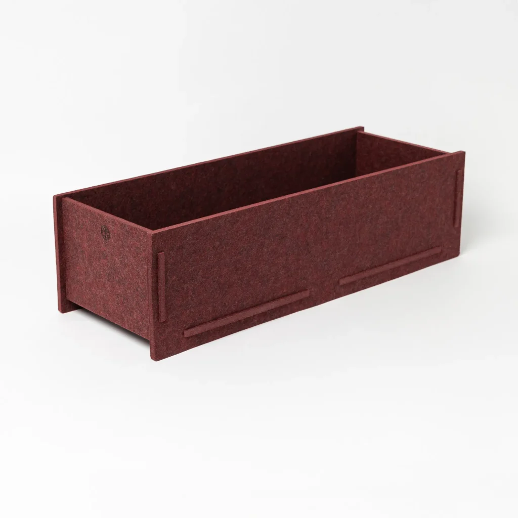 WoodUpp rectangular felt planter box in deep burgundy, shown empty on a white background. The minimalist storage/planter features interlocking felt panels, raised edge feet and subtle WoodUpp logo on one end, showcasing soft textured material and clean, modern lines for desktop or shelf use.