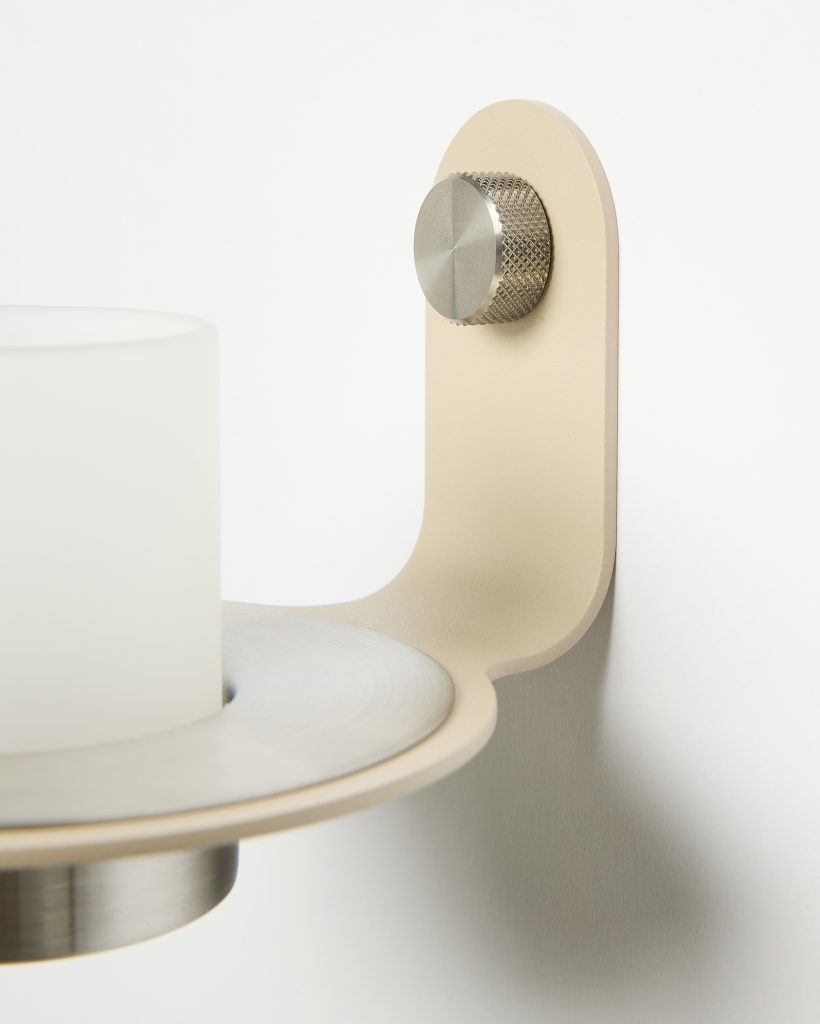 WoodUpp wall sconce featuring a matte beige powder-coated metal bracket with rounded arm, a brushed stainless steel circular plate and knurled adjustment knob, and a frosted glass votive cup resting in a recessed metal holder. Minimal, modern design in neutral tones suitable for candle or LED placement.