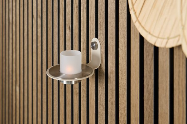 WoodUpp slatted wall panels in natural oak with black recessed grooves frame a minimalist steel wall-mounted candle holder from WoodUpp, featuring a brushed-metal plate and frosted glass LED tealight; the warm wood grain contrasts with the cool metallic sconce, creating a modern, cozy accent.